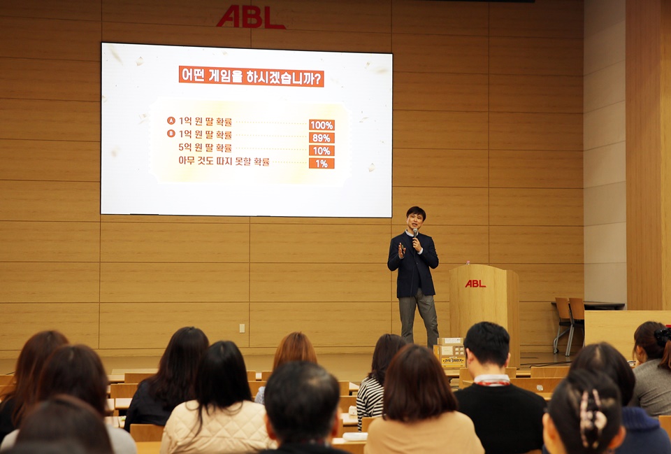 김태훈 교수가 어떤 게임을 하시겠습니까?, A : 1억 원 딸 확률 100%, B : 1억 원 딸 확률 89%, 5억 원 딸 확률 10%, 아무 것도 따지 못할 확률 1%가 쓰여진 화면을 보여주면서 질문을 하고 있는 강의 모습의 사진